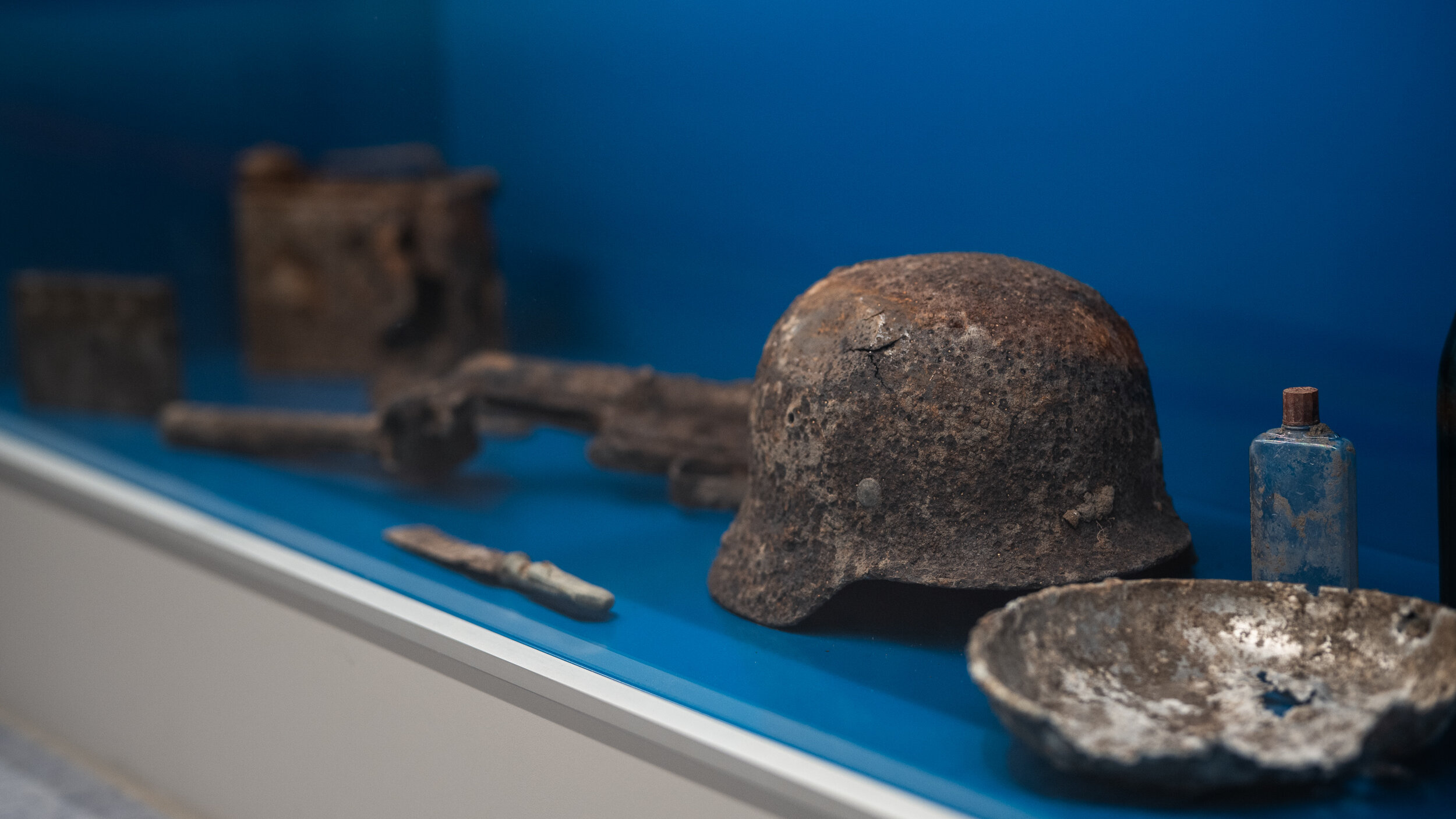 In einer Vitrine mit blauem Hintergrund liegen verschiedene Bodenfunde, unter anderem ein Stahlhelm. 