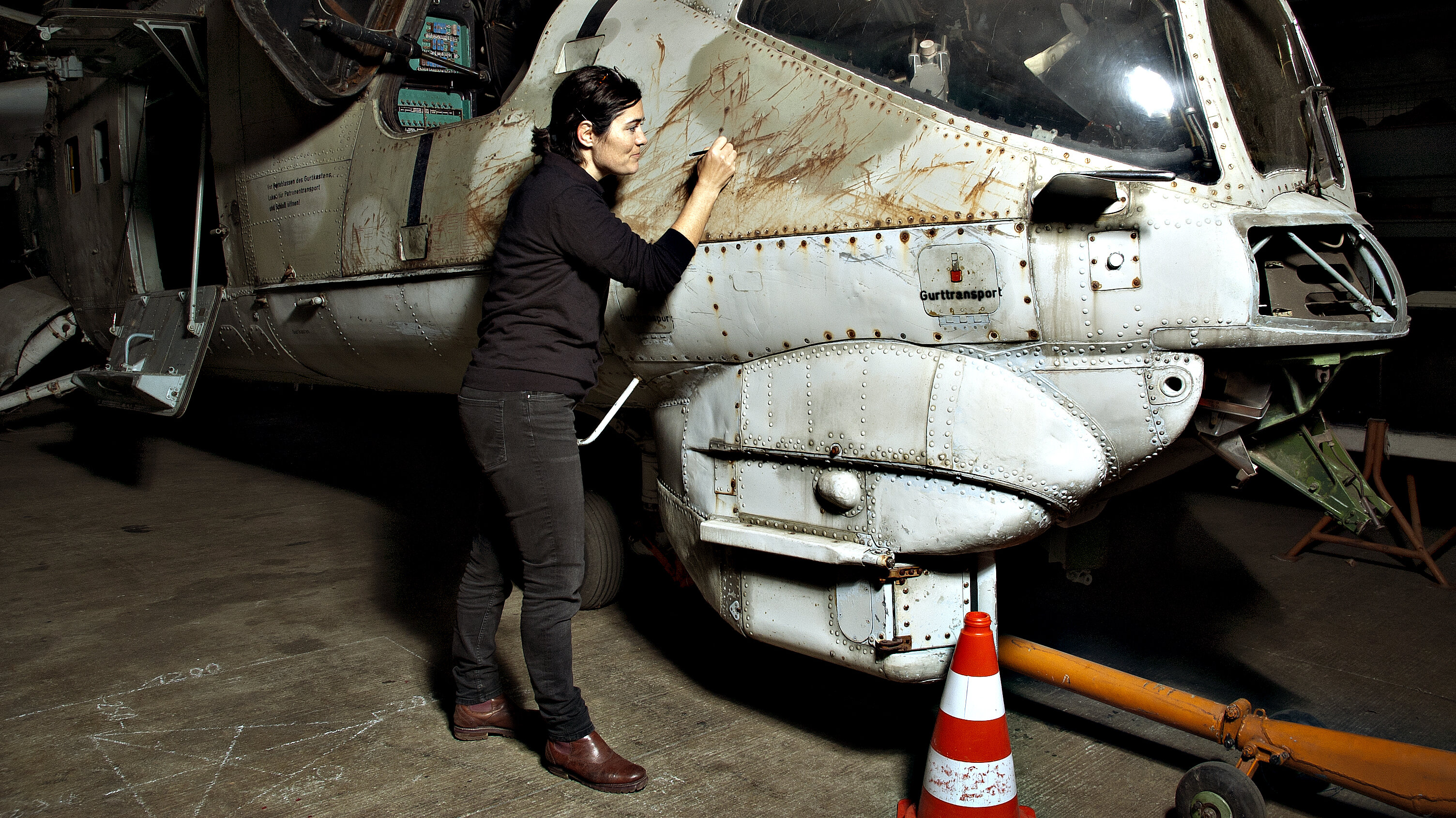 Eine Restauratorin arbeitet außen am Cockpit eines Helikopters und behandelt Kratzspuren. 