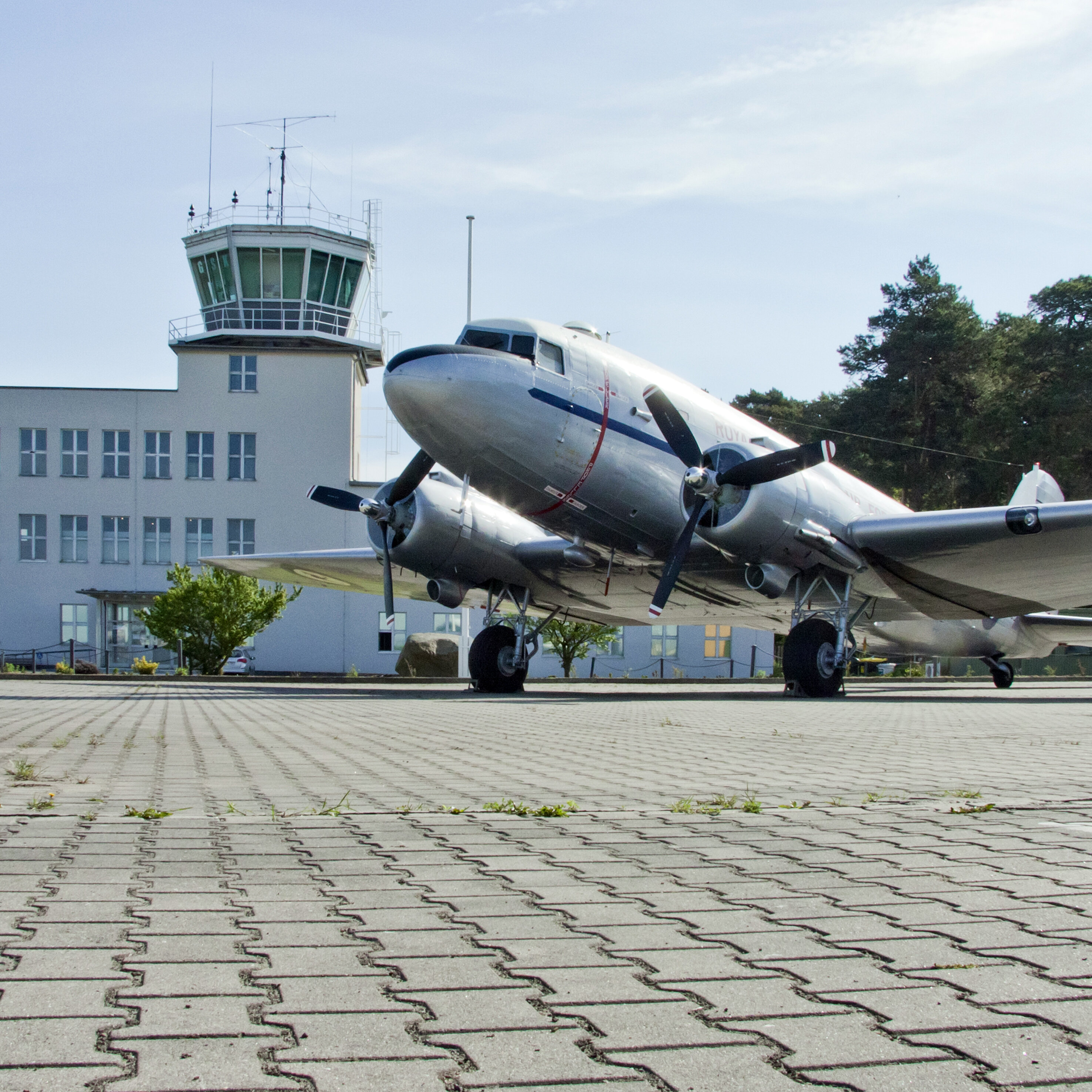 The picture shows an aeroplane in front of the control tower.