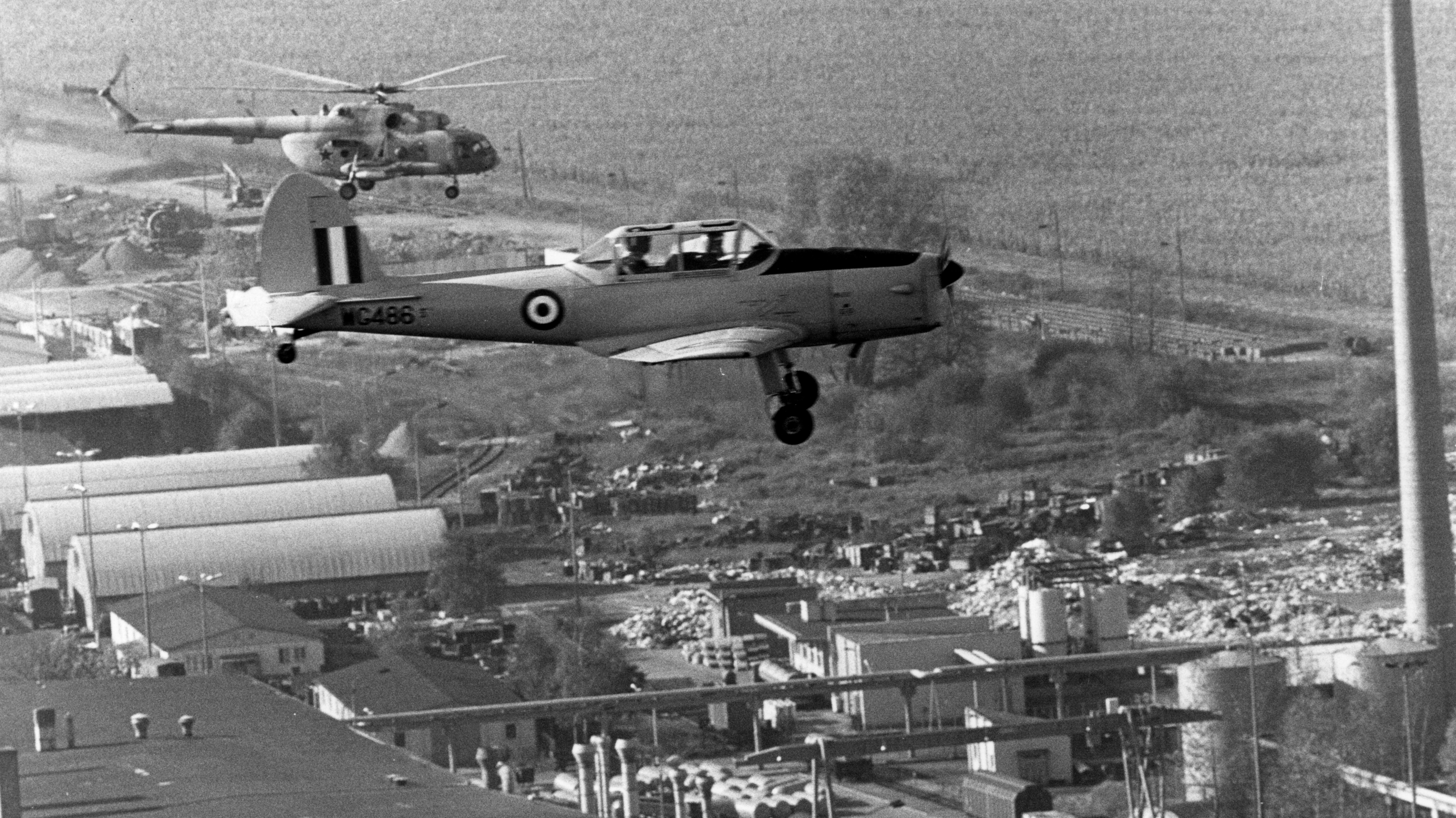 Ein einmotoriges zweisitziges Flugzeug und ein Hubschrauber fliegen sehr nah beieinander. 