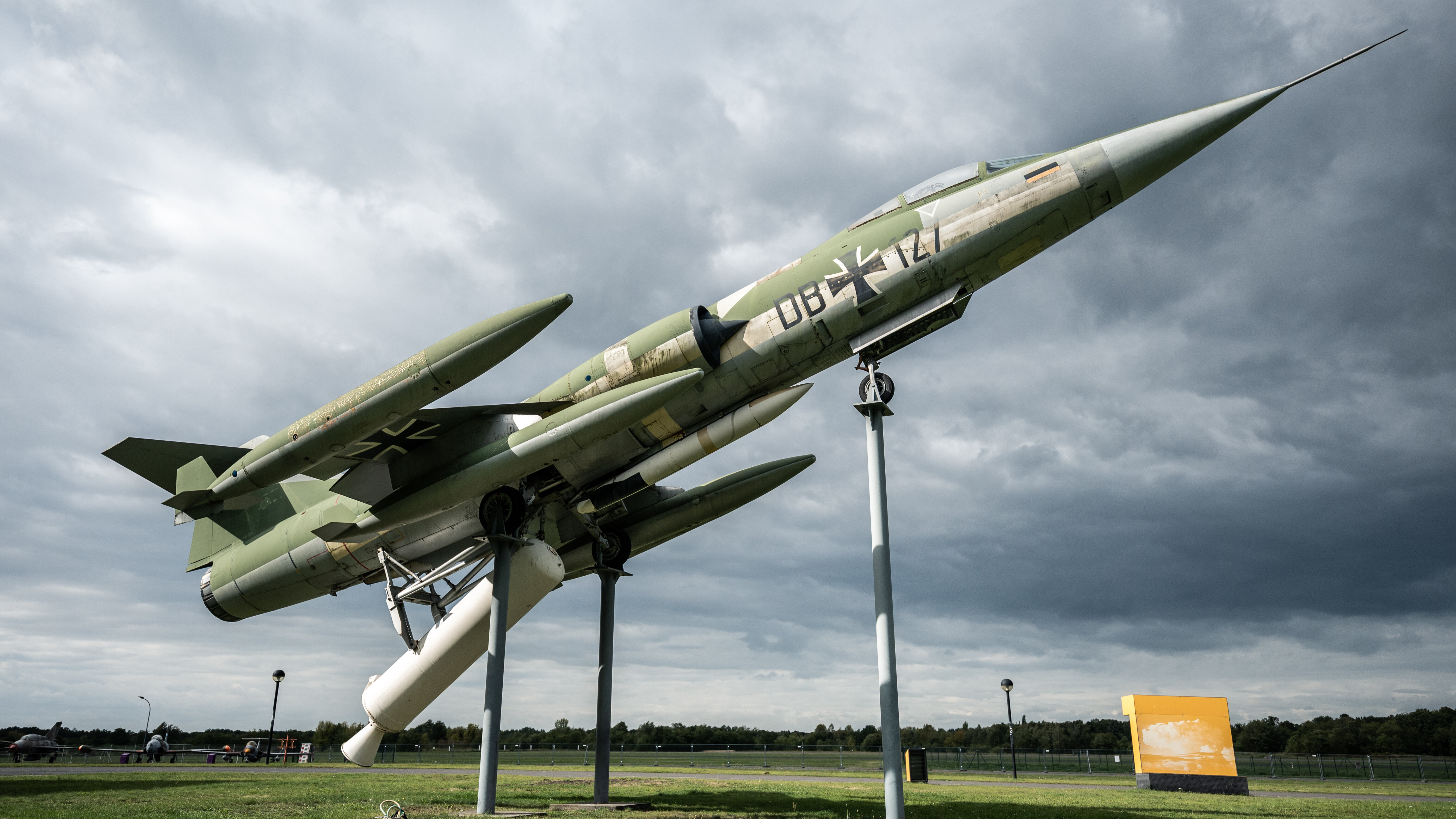 Stíhací letoun F-104 Starfighter na podpěrách ve startovní pozici před temnou oblohou s mraky.