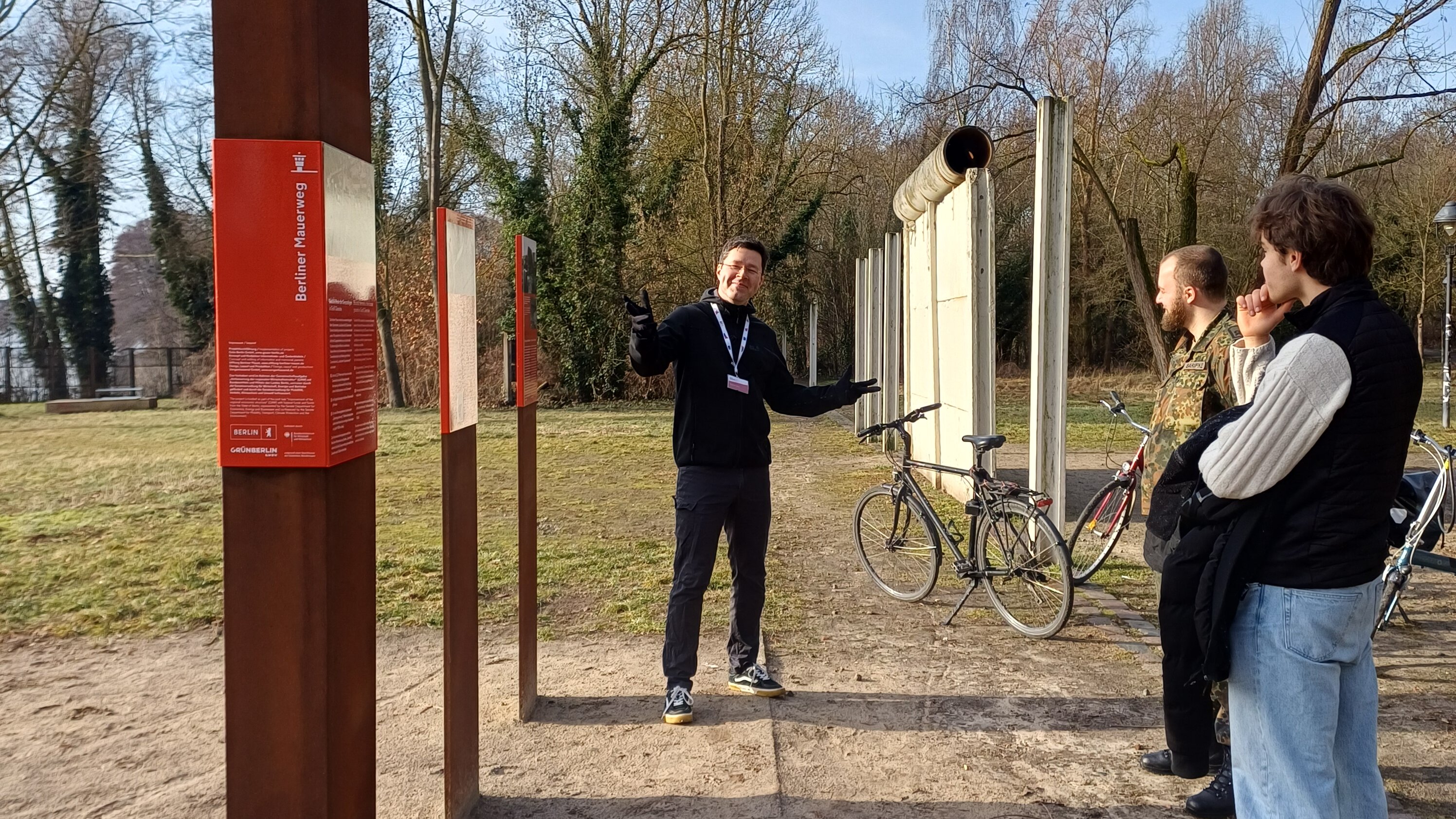 Guide erklärt zwei interessierten Männern den Berliner Mauerweg.  
