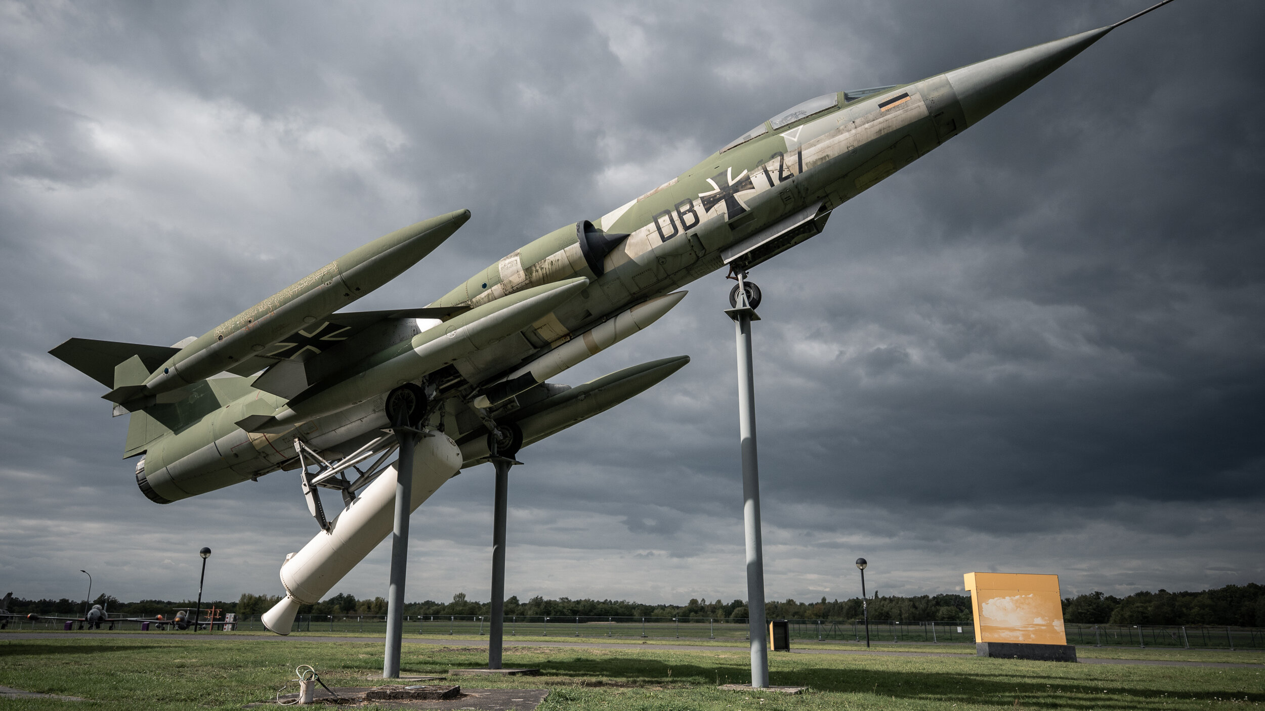 Das Jagdflugzeug F-104 Starfighter auf Stützen in Startposition vor dunklem Wolkenhimmel. 
