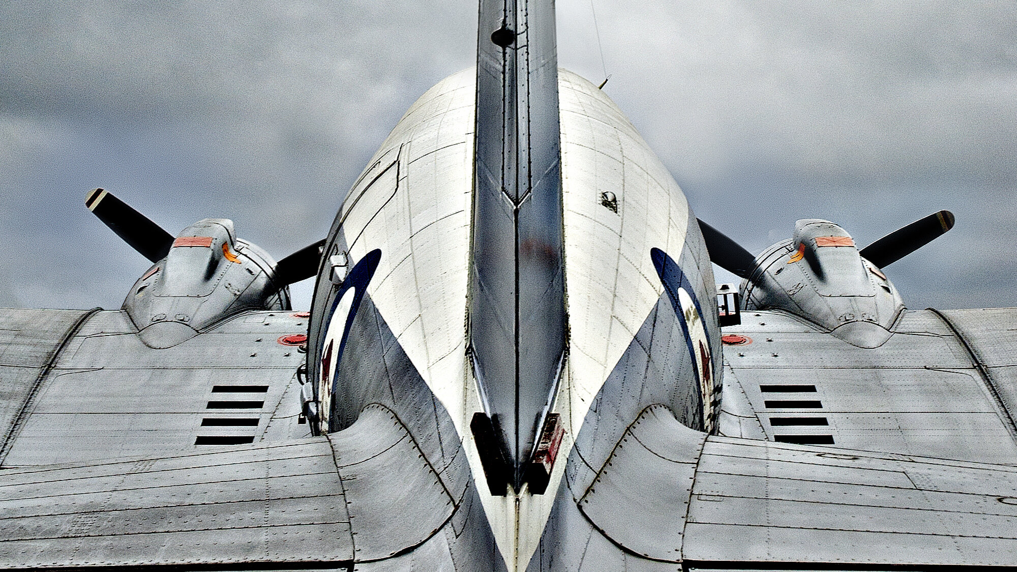 Symmetrische Heckansicht der Douglas C-47 mit hohem Seitenleitwerk unter grauem Himmel. 