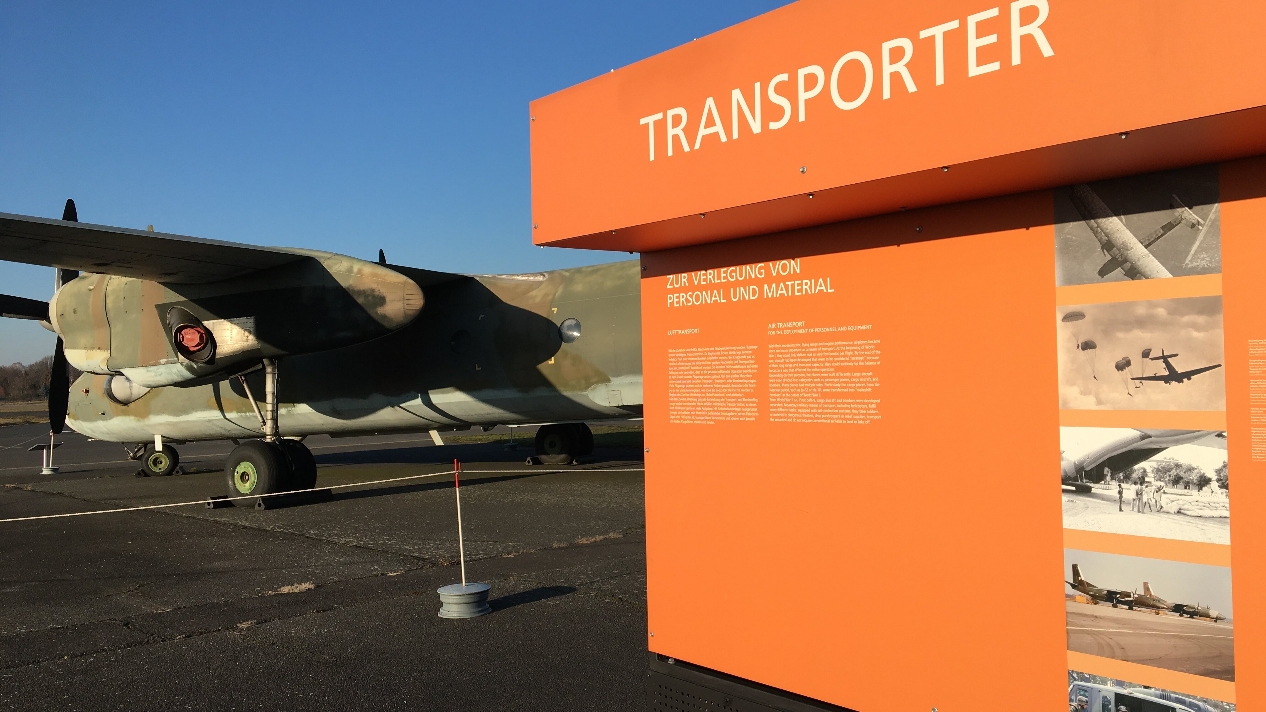 Orangefarbene Informationsstele zu Transportflugzeugen; links davon eine Antonov AN-26T in Teilansicht. 