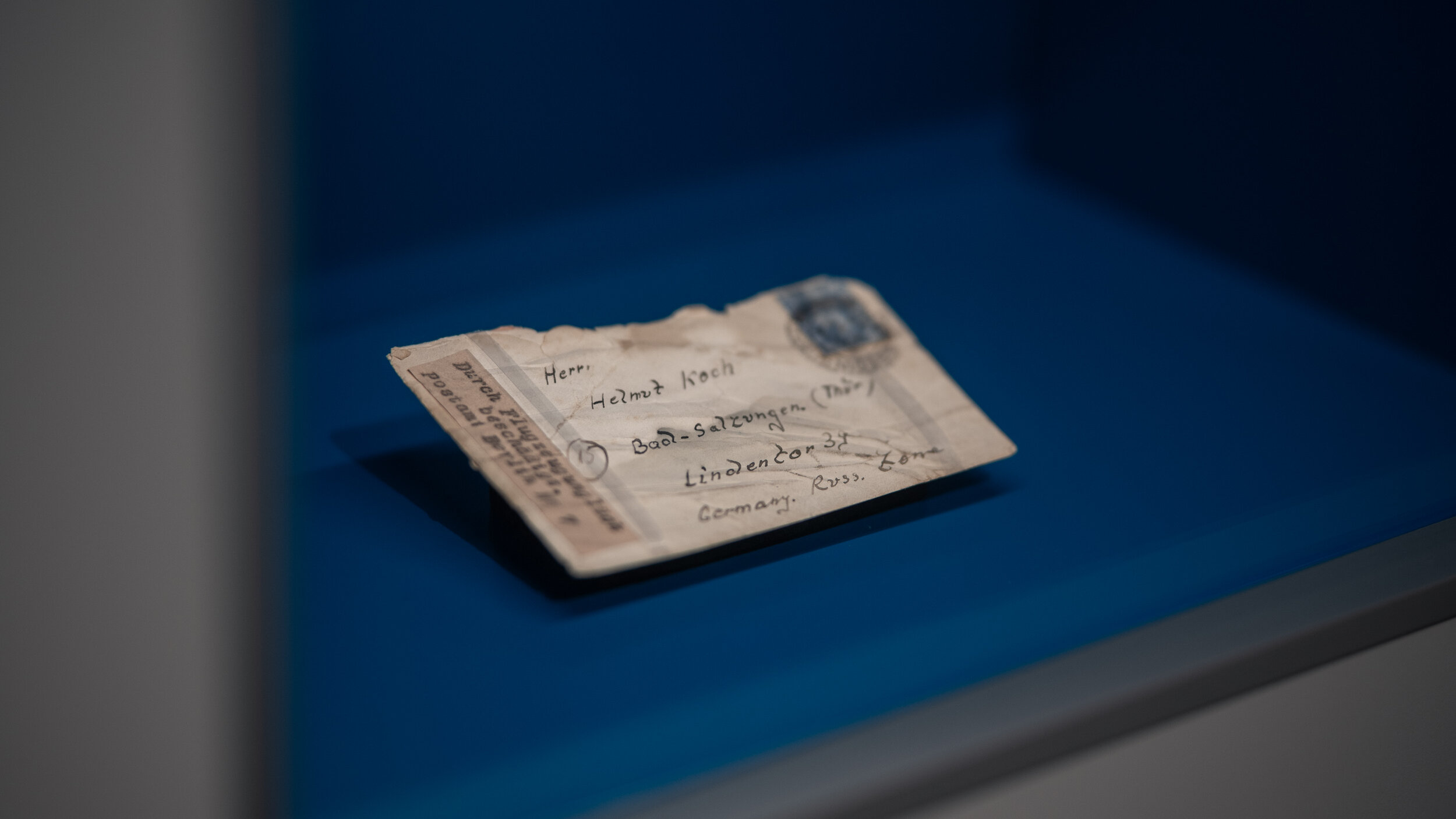 Ein beschädigter Briefumschlag liegt in einer Vitrine, auf dem vermerkt ist „Durch Flugzeugunglück beschädtigt“. 