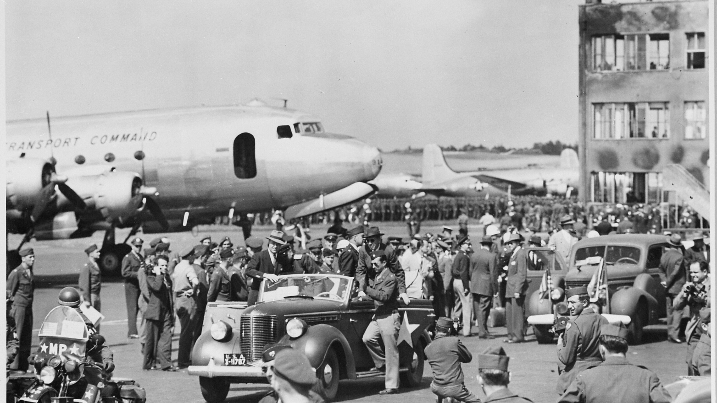 Viele Menschen auf dem Vorfeld, dazwischen Fahrzeuge, im Hintergrund ein Flugzeug und der Tower. 