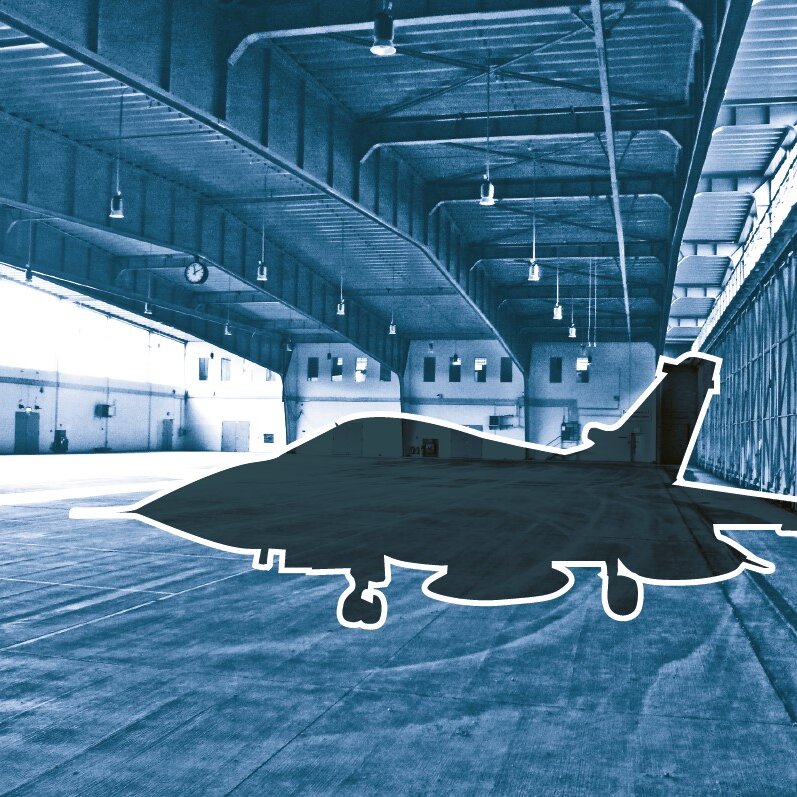 Blaugetöntes Foto von einem leeren Hangar, darin der Scherenschnitt eines Kampfflugzeugs 