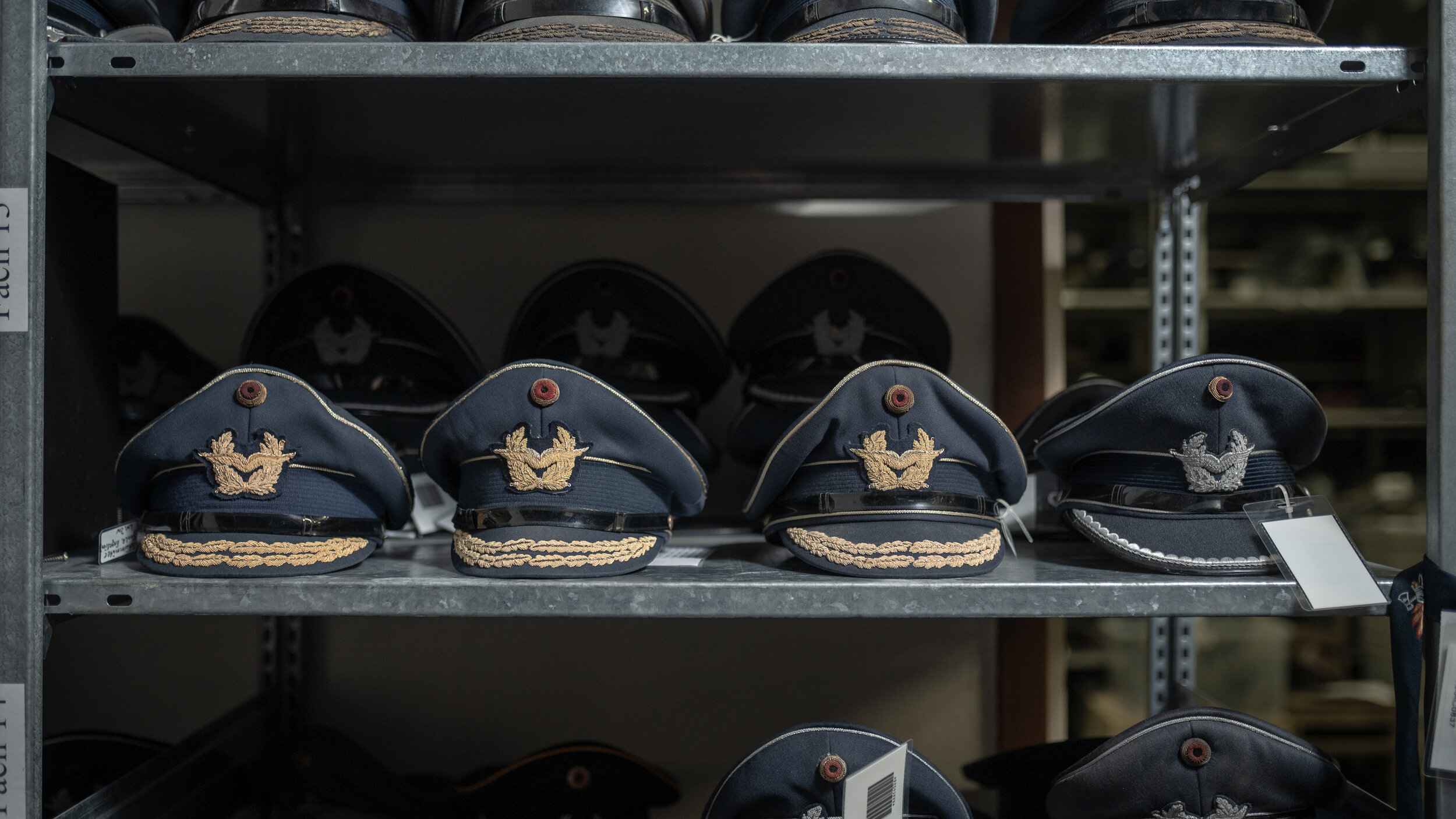Mehrere Reihen blauer Uniformmützen der Luftwaffe der Bundeswehr mit Adleremblem, gelagert in Metallregalen im Depot. 