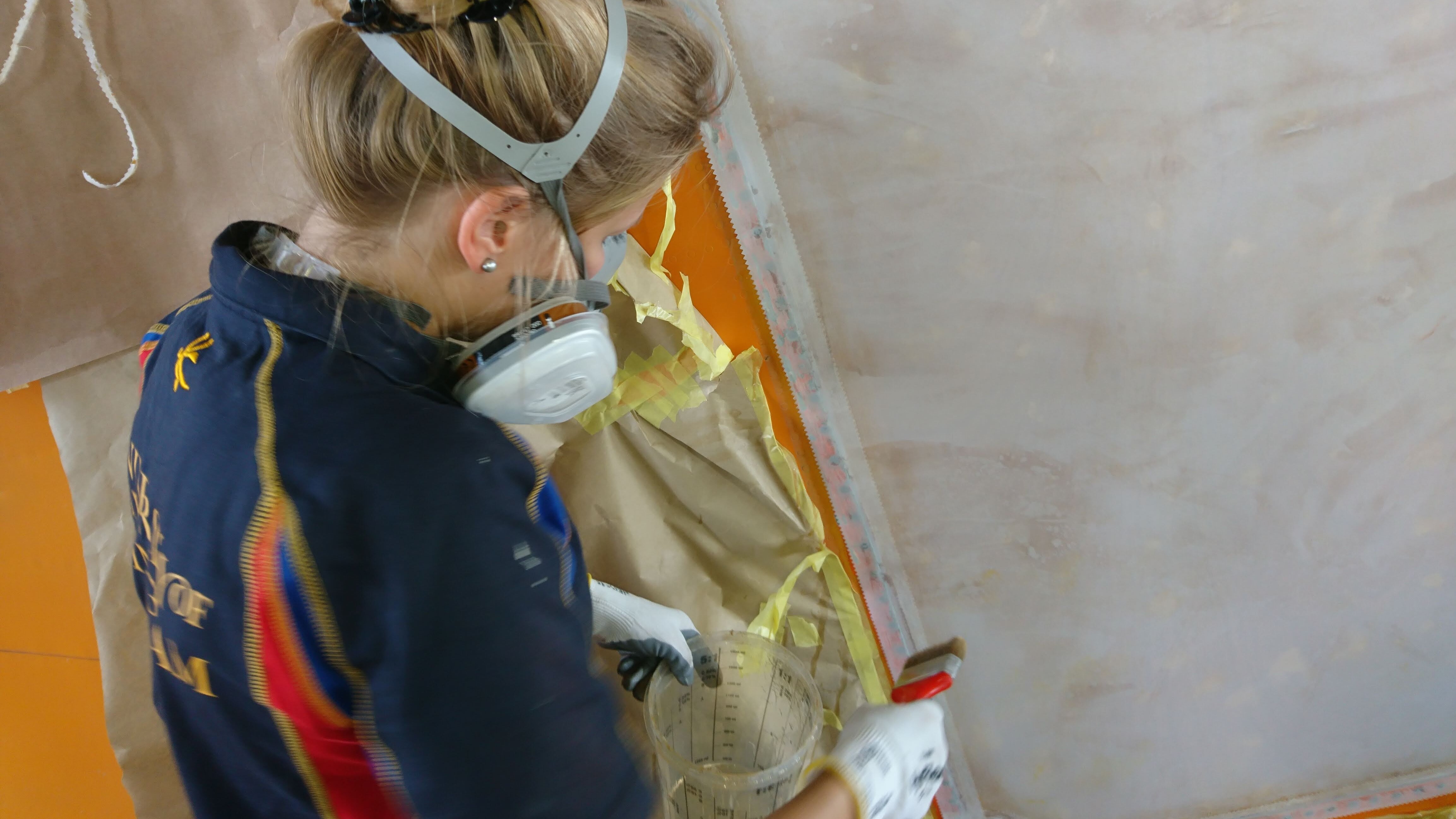 Eine Restauratorin mit Mundschutz arbeitet an einem Flugzeugleitwerk. 